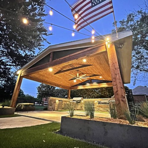 A modern metal patio cover with a flat roof and two beams, attached to a white house with sliding glass doors and a concrete floor.