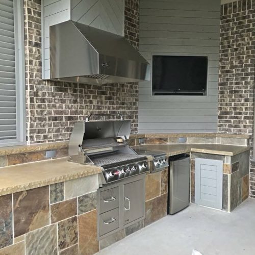 Outdoor living kitchen set in a spacious backyard in Flower Mound, Texas, 75022 featuring stainless steel appliances, stone countertops, and a built-in grill.